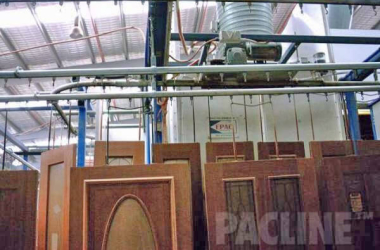 Large wooden doors hang from Pacline enclosed track conveyor to transport from finishing through assembly process