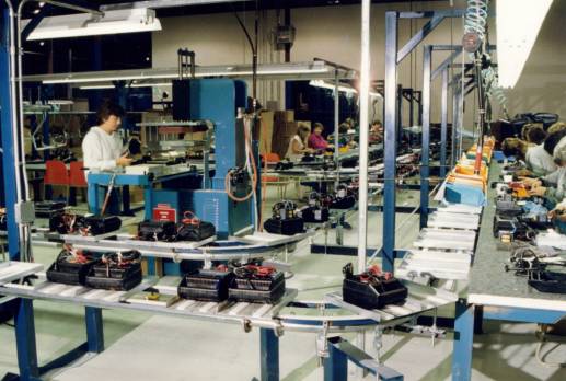 Inverted assembly line conveys battery chargers.