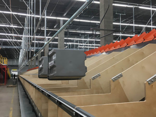 Empty tote conveyor delivering totes to operators at chutes from a tilted tray sorter.