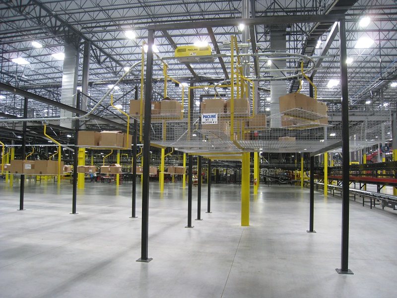 Overhead monorail conveyor transports totes and corrugated cartons in large distribution center.