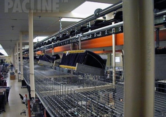 Moving beverage bottle bags from warehouse to assembly onto bottles using enclosed track conveyor system.