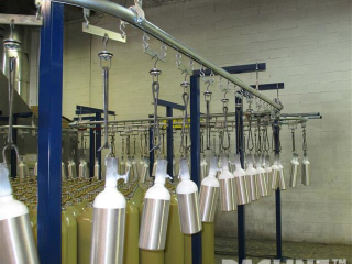 Overhead conveyor system for automating wet spray painting of propane tanks.