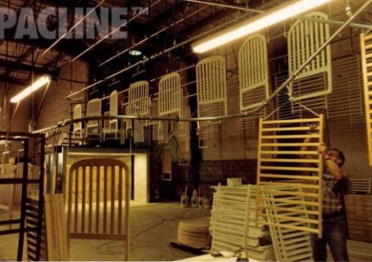 Monorail enclosed track conveyor moves wooden bed frames through sanding and paint finishing.